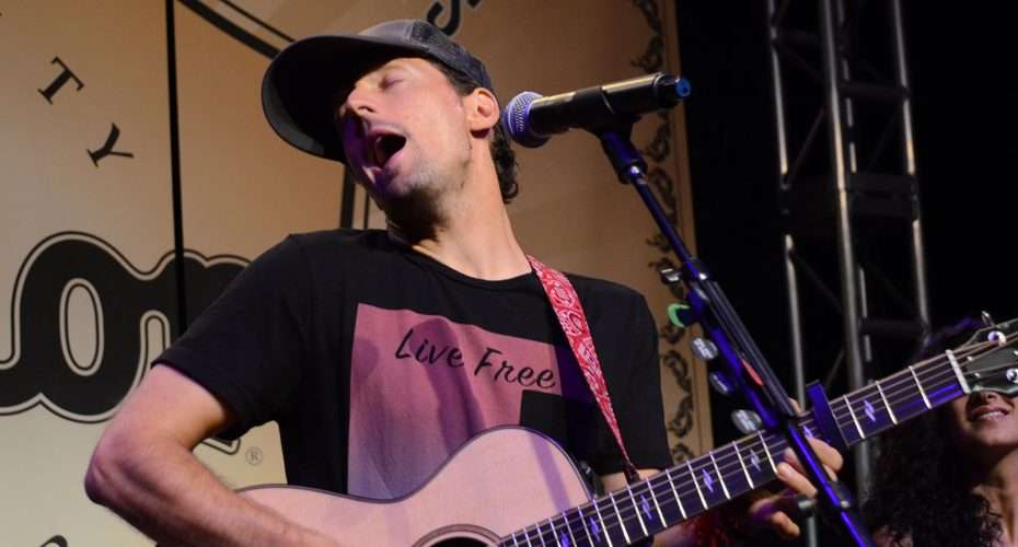 Musician with Taylor guitar and Lectrosonics mic on NAMM stage, "Live Free" shirt