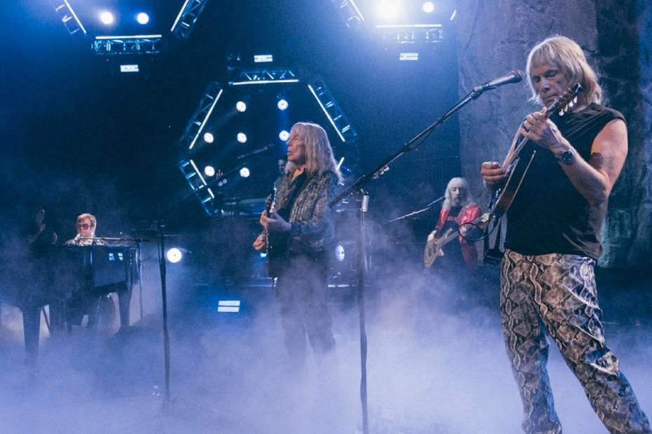 Spinal Tap II band members perform on stage with fog and lighting.