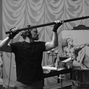 Sound recordist with boom mic near artwork, possibly for Hallmark project.